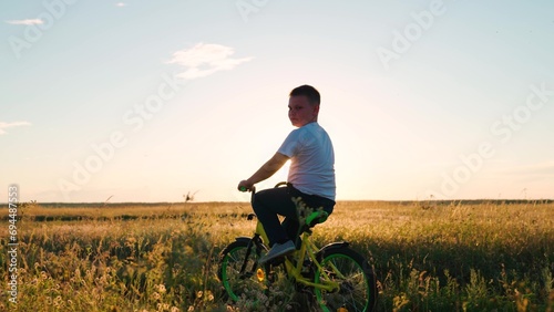Child boy rides bicycle on grass field. Childs feet are pedaling. Child, cyclist plays, rides, sunset. Pedaling, bicycle wheel. Childrens travel. Physical exercise. Family in park. Kid play lifestyle