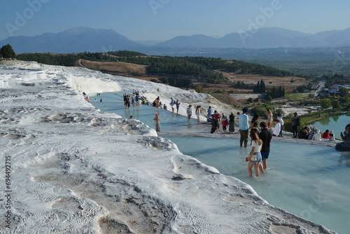 Visitors experience the healing properties of the white travertine natural thermal pools of Pamukkale, Turkey, famous for their healing properties, rich in minerals like sulfur and silica.