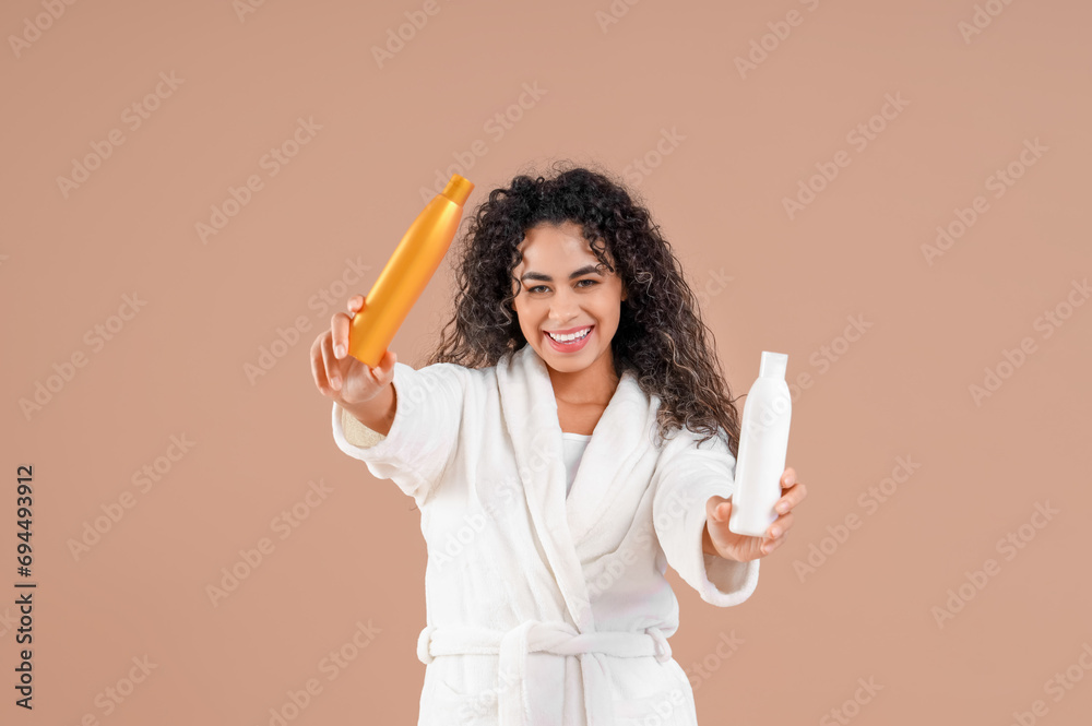 Young African-American woman in bathrobe with bottles of shower gel on brown background Young African-American woman in bathrobe with bottles of shower gel on brown background