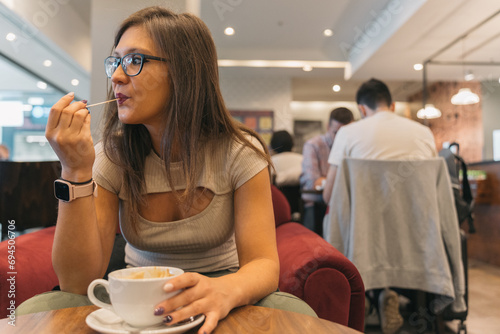 Young woman savoring coffee. Anonymous girl stirring the coffee with a stick and tasting the delicious foam. photo