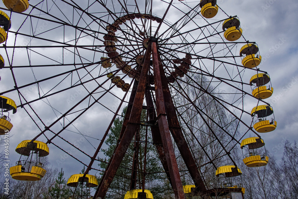 A rusted Ferris wheel with yellow cabins against a cloudy sky. A rusted Ferris wheel with yellow cabins against a cloudy sky.