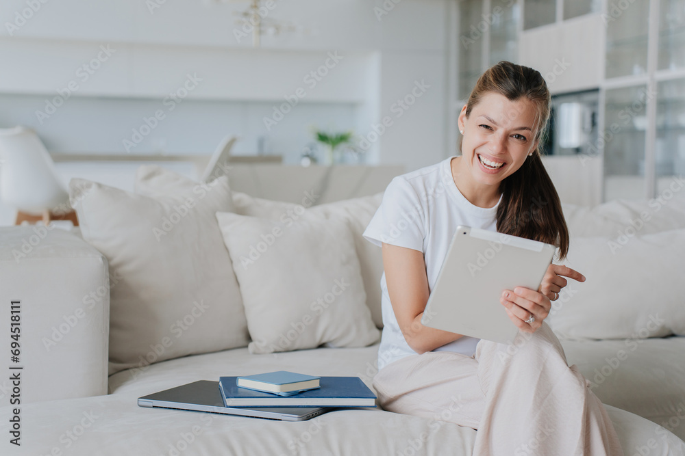 cheerful woman in casual attire enjoys using a tablet on a comfortable sofa in a bright, airy living room, surrounded by plush cushions, exuding a sense of casual leisure and digital connectivity cheerful woman in casual attire enjoys using a tablet on a comfortable sofa in a bright, airy living room, surrounded by plush cushions, exuding a sense of casual leisure and digital connectivity