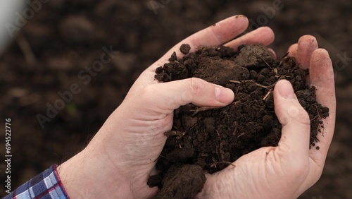 Fertile soil in male hands of farmer. Male hands hold fertile land in field. Organic soil in hands of farmer at sunset in field, natural farming. Agricultural business concept. Humus, fertilized land