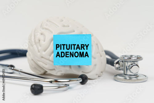 On a white surface next to the stethoscope lies a brain on which a sticker with the inscription - Pituitary adenoma photo