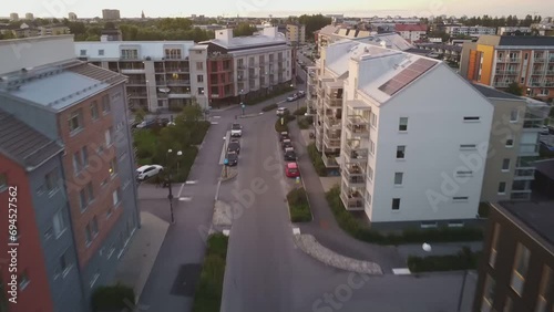 A car slowly driving home between Swedish apartment buildings at sunset as seen from behind and in the air