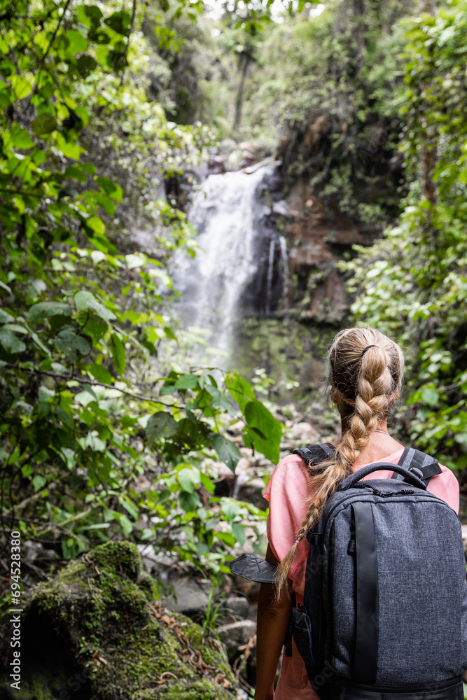 Rear view of blonde woman hiker watching waterfall inside rain forest in Panama