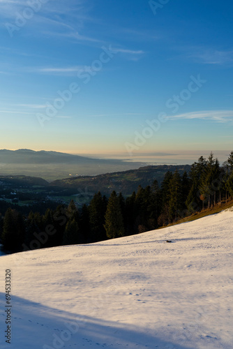 View from snowcovered mountain down onto a lake in evening light