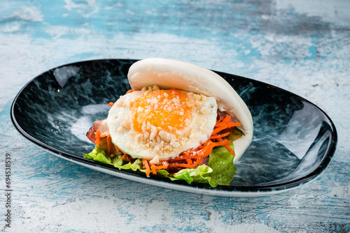 Flatbread with bacon, fried egg, carrots, lettuce and cheese in a plate. photo