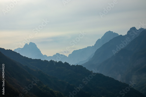 Panoramic view of mountain silhouette seen along the Alpe Adria trail in Friuli-Venezia Giulia, Italy, Europe. Dawn reveals a serene landscape - fog, mystical mountains, forests, and beauty in nature.