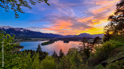Panoramic sunset view on Lake Faak from Taborhoehe in Carinthia, Austria, Europe. Surrounded by high Austrian Alps mountains. Water surface reflecting soft sunlight. Remote alpine landscape in summer photo