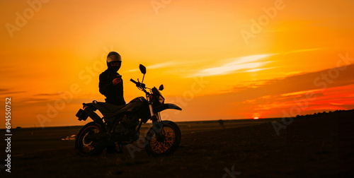 silhouette of a male motorcyclist at sunset and an off-road enduro cross-country motorcycle. © velimir