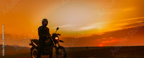 silhouette of a male motorcyclist at sunset and an off-road enduro cross-country motorcycle.