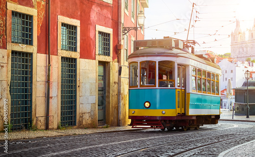 Lisbon Portugal. Vintage retro tram driving by street of paving stones in district Alfama. Cityscape panorama with old houses and tower sunny day