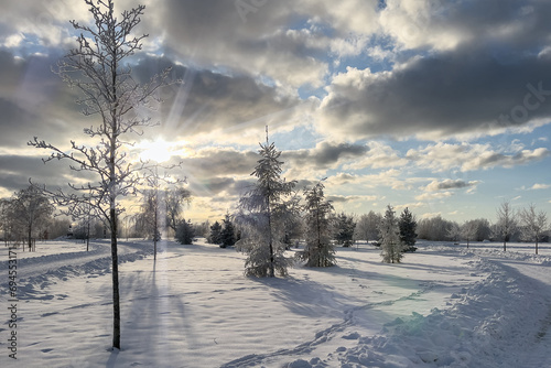 Sunny and cold winter day in the city park. Lots of snow, deep snow, cloudy skies and sun rays through the clouds
