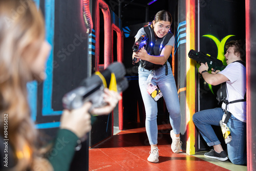 Smiling girl with laser pistol during playing laser tag with her friends in dark room