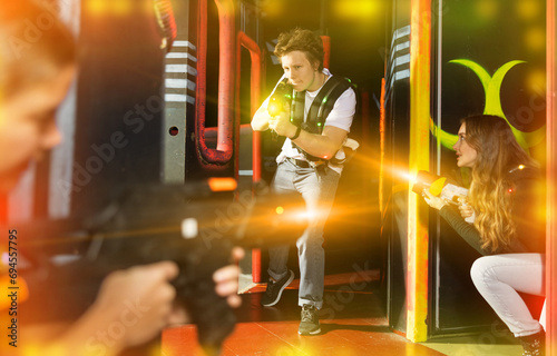 Portrait of positive young man with laser gun having fun with her friends on lasertag arena