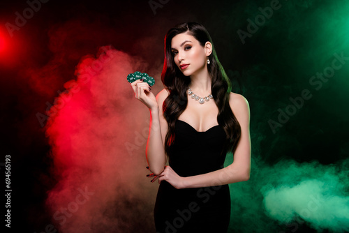 Photo of classy lady croupier in private vip poker club show chips for another game over mist neon dark background photo