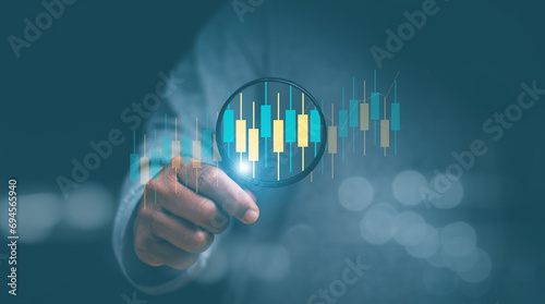 Finance and investment data search concept. Businessman hand holding magnifier and zooming at candlesticks bar chart of stock market data. Stock market analyzing, stock information search.