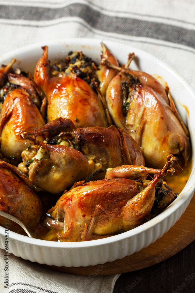 Baked quail stuffed with mushrooms, eggs and bread in a ceramic form on a wooden table.
