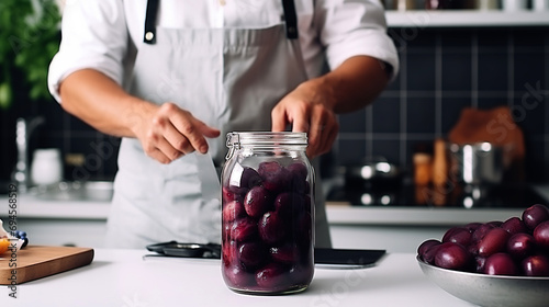 A male chef prepares plum compote on a table in the kitchen. Male hands on the background of a home kitchen. Preparing plum dessert. A man fills a jar with plums. photo