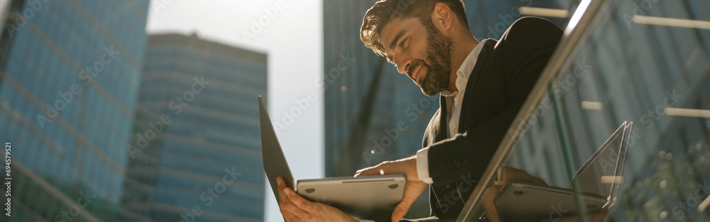 Handsome businessman working on laptop standig on office terrace - obrazy, fototapety, plakaty 
