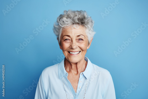 Portrait of happy senior woman smiling at camera on blue background.