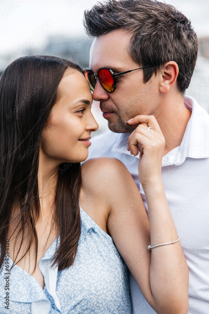 A young woman and a stylish man are facing each other. Portrait of a happy couple in love. A man in sunglasses enjoys a walk with his beloved woman
