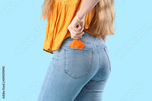 Young woman with condom in pocket on blue background, closeup