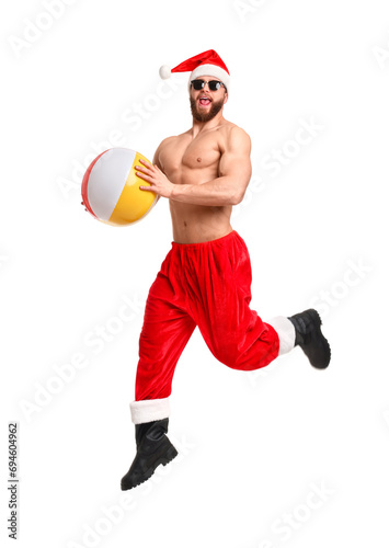 Fototapeta Naklejka Na Ścianę i Meble -  Muscular young man in Santa hat with ball jumping on white background