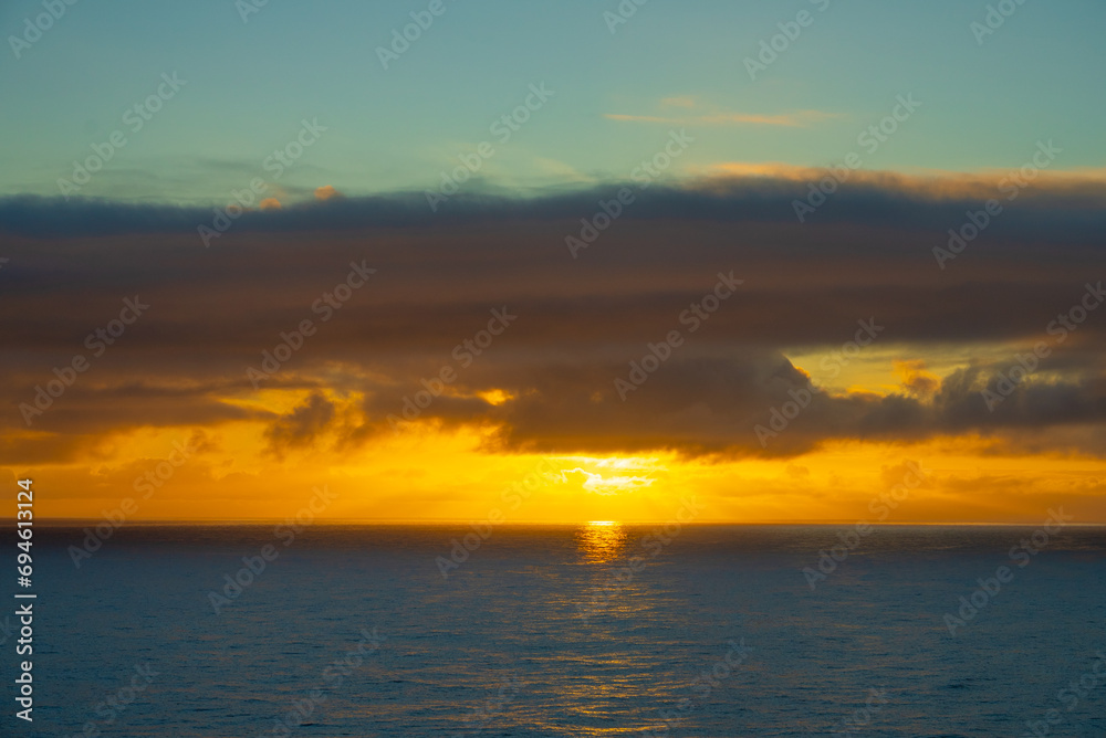 A Coastal Canvas Unfurls as Clouds Soften the Sun's Fiery Goodbye over the Ocean Horizon