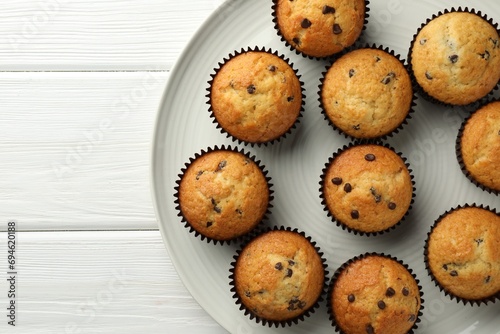 Delicious freshly baked muffins with chocolate chips on white wooden table, top view