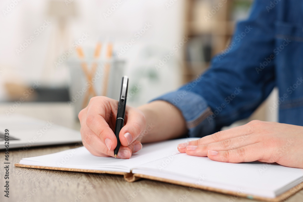Young woman writing in notebook at wooden table, closeup Young woman writing in notebook at wooden table, closeup