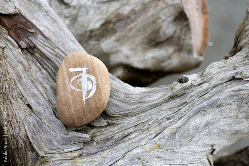 A close up image of a healing reiki symbol and white sage smudge stick on a weathered and worn piece of driftwood with an ocean background. 