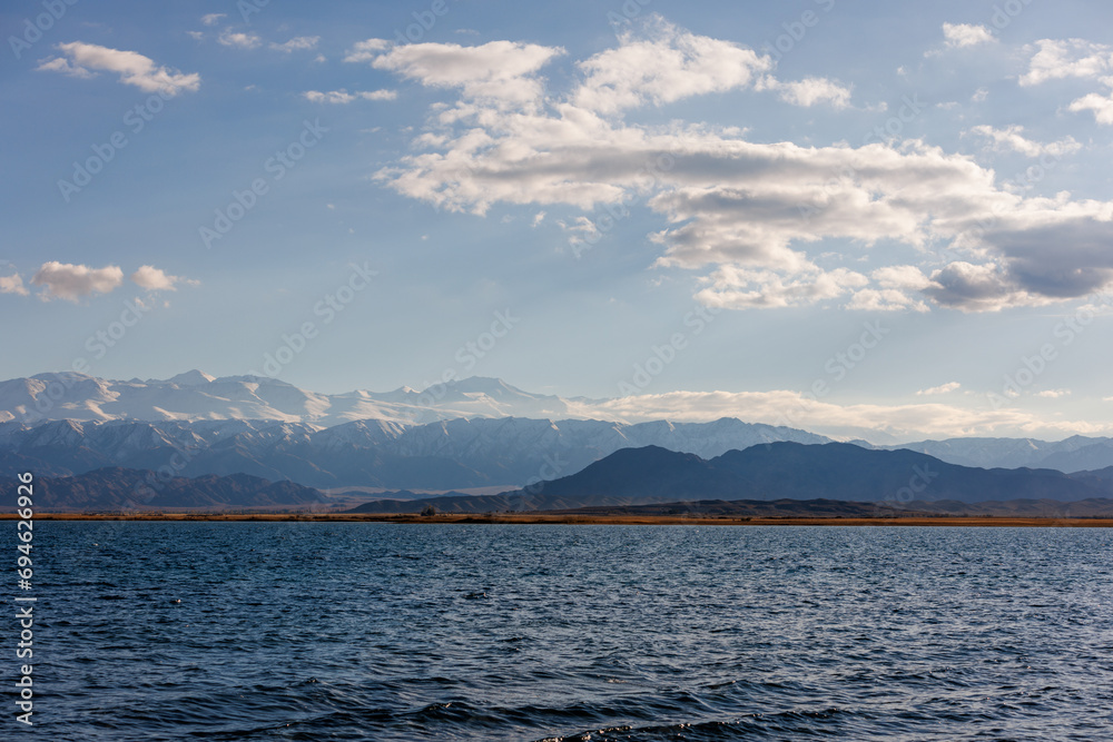 Blue calm water in Issyk-Kul lake with mountains on background at autumn afternoon.