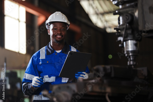 Portrait male African American workers wearing uniform safety and hardhat using tablet working at machine in factory Industrial. Engineering worker man work machine lathe metal. photo