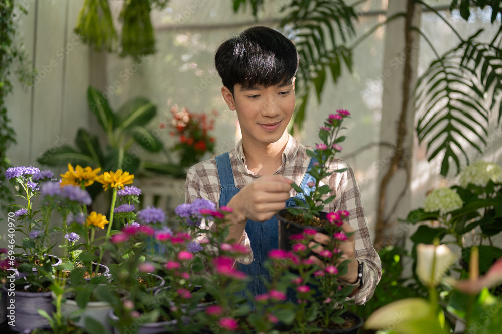 Young positive Asian male florist is working at plant nursery and taking care of the potted flowers.