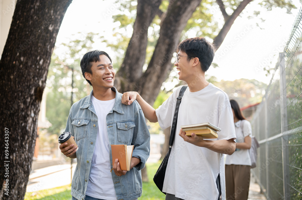 Two young Asian male best friends are enjoying talking while walking on a footpath on their campus. Two young Asian male best friends are enjoying talking while walking on a footpath on their campus.