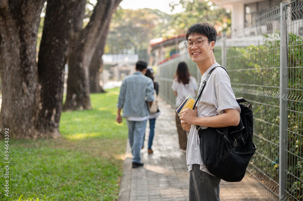 Positive Asian male student with backpack is walking to school, walking on a footpath on his campus. Positive Asian male student with backpack is walking to school, walking on a footpath on his campus.