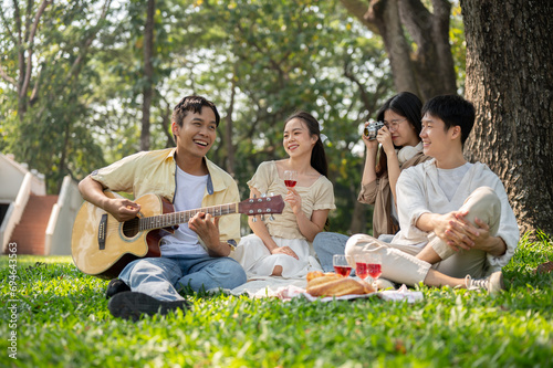 Group of cheerful diverse young Asian friends are enjoying picnicking in a beautiful park together.