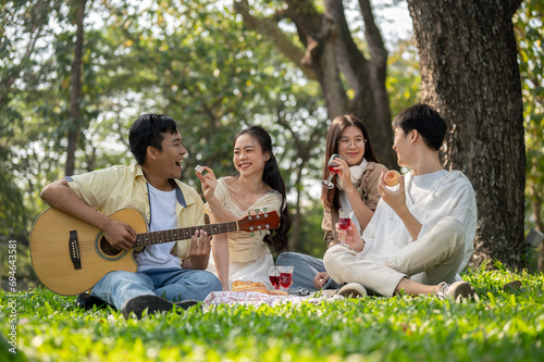 A group of happy and positive young Asian friends is enjoying picnicking in a green park together.