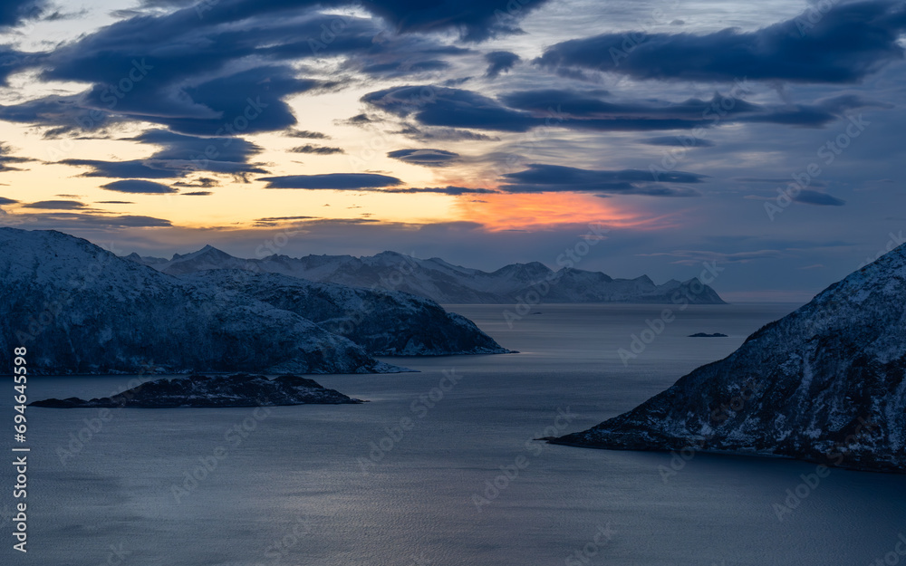 Ośnieżone wybrzeże w Norwegii, skalisty fiord w o zachodzi słońca