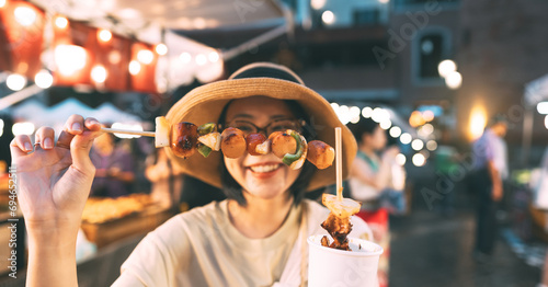 Focus on barbeque asian foodie woman eating bbq grilled skewers at outdoor night market street food photo
