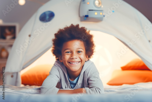 Joyful afro american child lying on his stomach inside a cozy blanket-forte resembling a space theme, with stars and a rocket ship, suggesting playful adventure and wonders of child's imagination