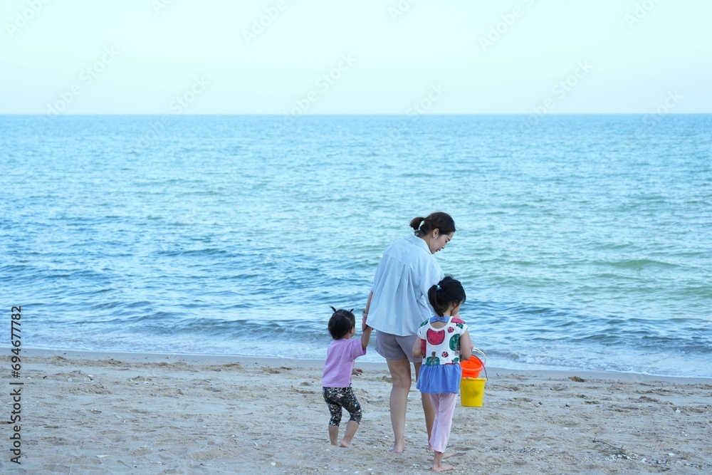 Afternoon beach front with a family tourist ,mother hand holding her childs  walking along the beach,one child hand holding bucket for sand playing ,beautiful beach front at Cha-am beach , Phetchaburi