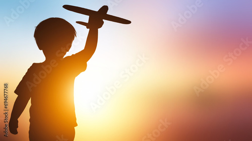 Quadro su tela Silhouette of a boy playing with toy airplane on sunset background