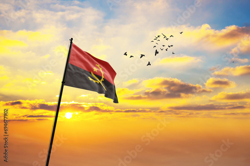 Waving flag of Angola against the background of a sunset or sunrise. Angola flag for Independence Day. The symbol of the state on wavy fabric.