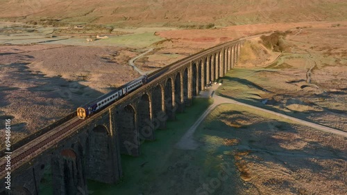 Train with two carriages crossing viaduct bridge on cold winter morning. Flight across tracks. 50 FPS. Ribblehead Viaduct, North Yorkshire, England, UK. photo