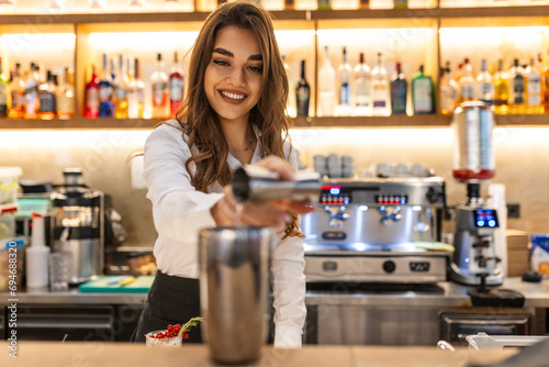 Beautiful female bartender pouring alcohol into shot glass shelves full of bottles with alcohol on the background © Graphicroyalty