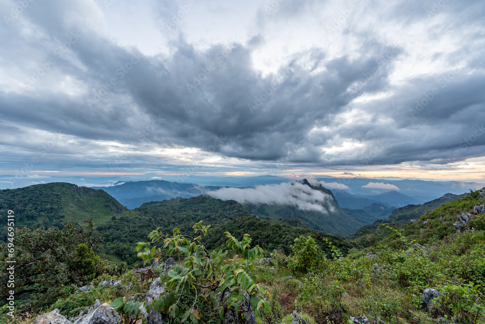 View from the top of Doi Luang Chiang Dao during an evening sunset with trees and shrubs in the foreground and dramatic clouds formation in background