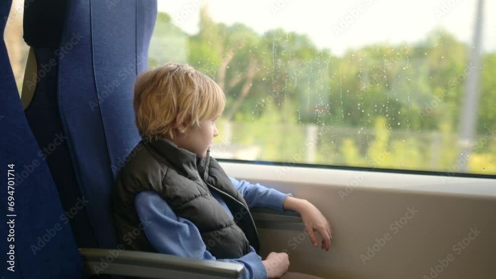 Cute preteen boy is traveling in a local train carriage or by railroad while it rain outside. Portrait of child passenger.
